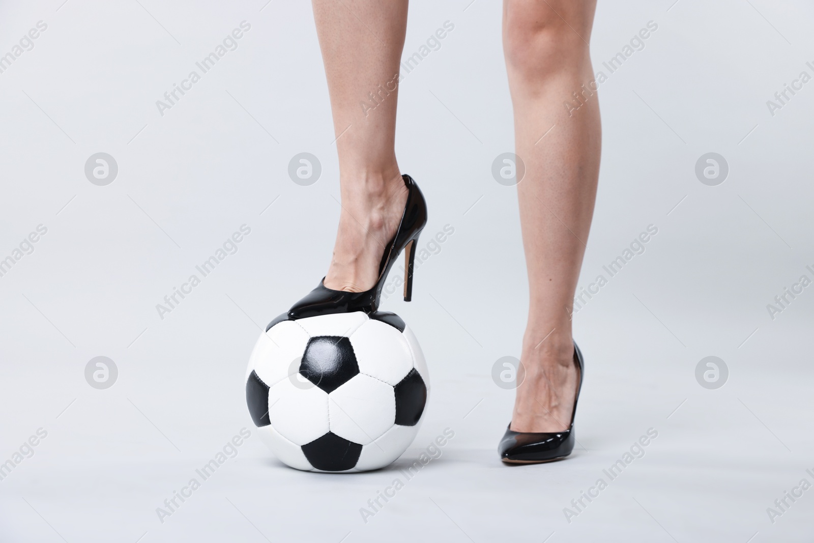 Photo of Woman in high heeled shoes with soccer ball on light background, closeup