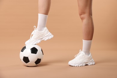 Photo of Woman in sneakers with soccer ball on beige background, closeup