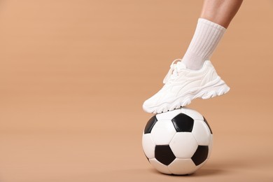 Photo of Woman in sneaker with soccer ball on beige background, closeup. Space for text