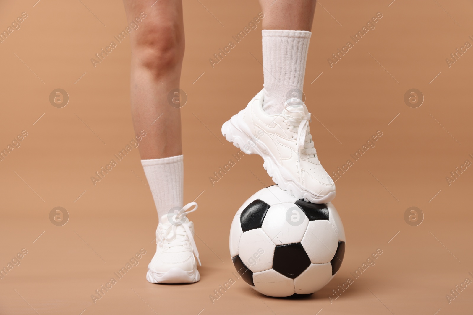 Photo of Woman in sneakers with soccer ball on beige background, closeup