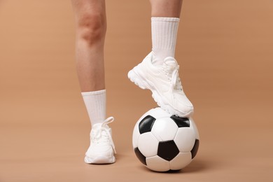 Photo of Woman in sneakers with soccer ball on beige background, closeup