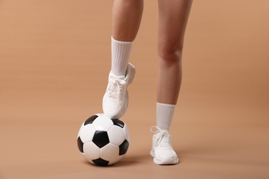 Photo of Woman in sneakers with soccer ball on beige background, closeup