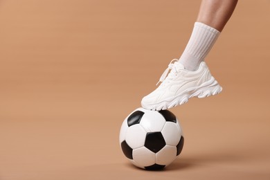 Photo of Woman in sneaker with soccer ball on beige background, closeup. Space for text