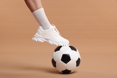 Photo of Woman in sneaker with soccer ball on beige background, closeup