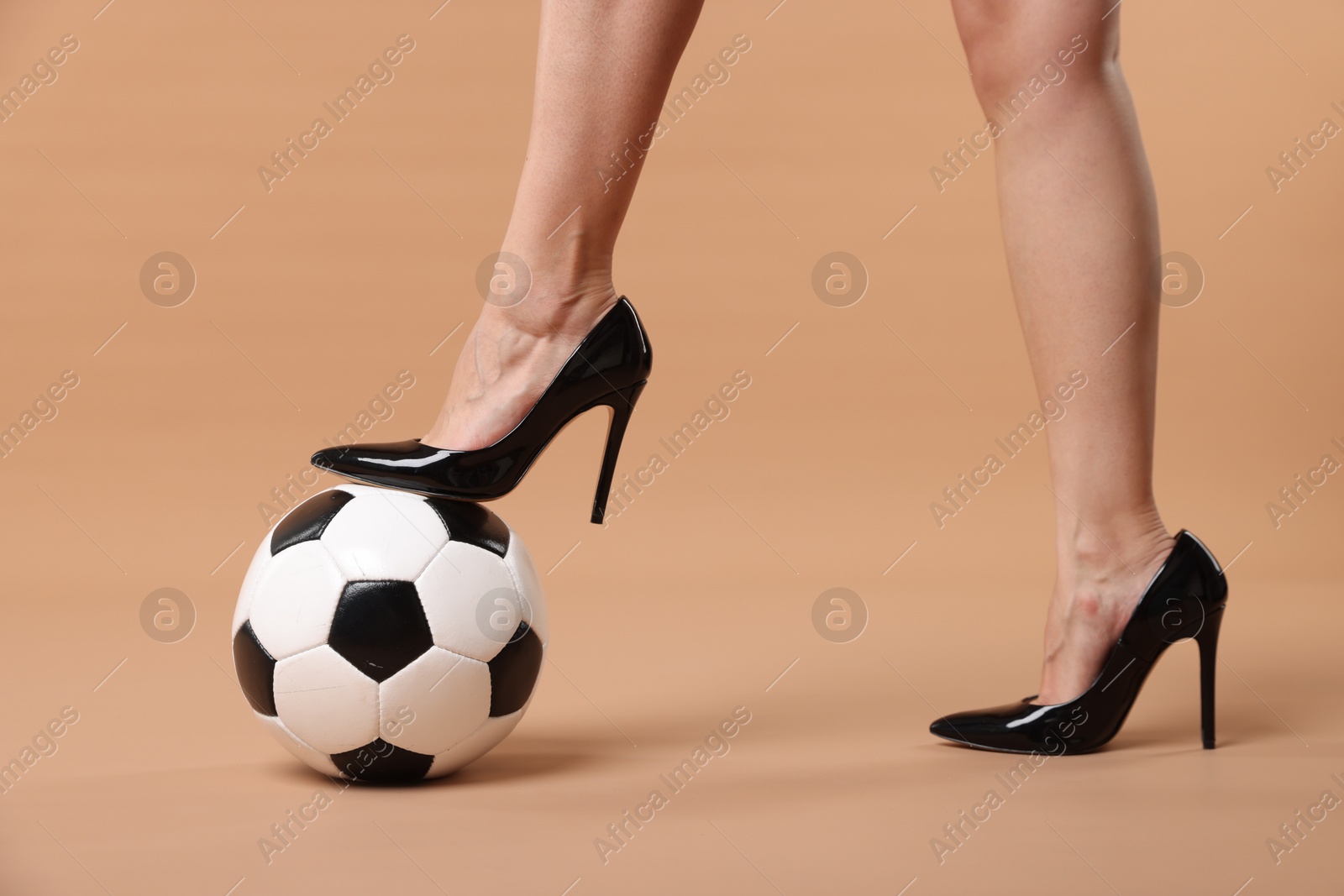 Photo of Woman in high heeled shoes with soccer ball on beige background, closeup