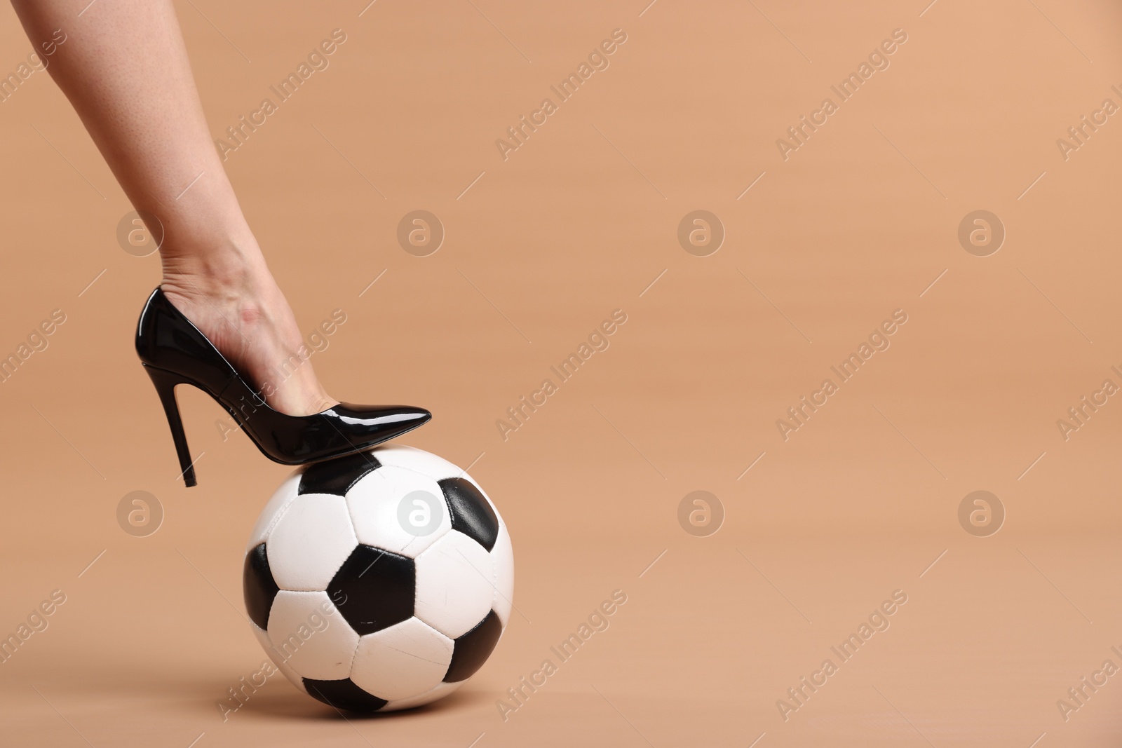 Woman in high heeled shoe with soccer ball on beige background, closeup. Space for text Photo of Woman in high heeled shoe with soccer ball on beige background, closeup. Space for text