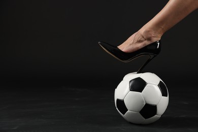 Photo of Woman in high heeled shoe with soccer ball on dark background, closeup. Space for text