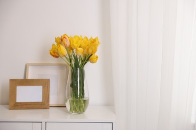 Photo of Bouquet of beautiful tulips and picture frames on table near white wall. Space for text