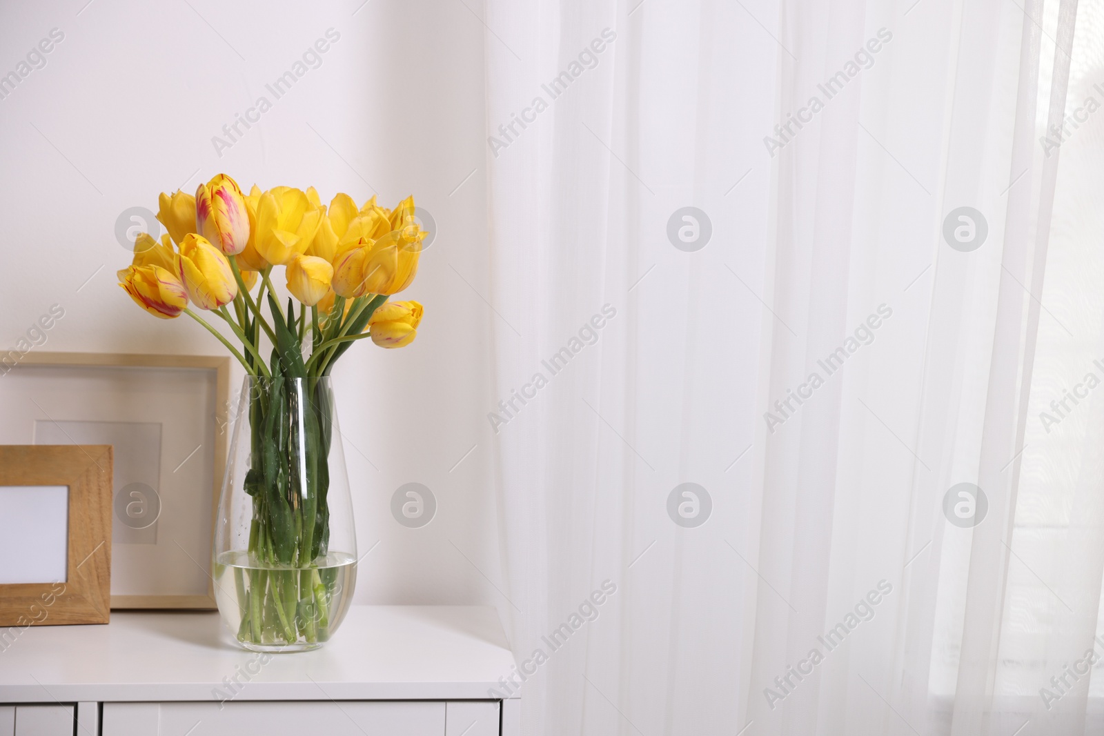 Photo of Bouquet of beautiful tulips and picture frames on table near white wall. Space for text