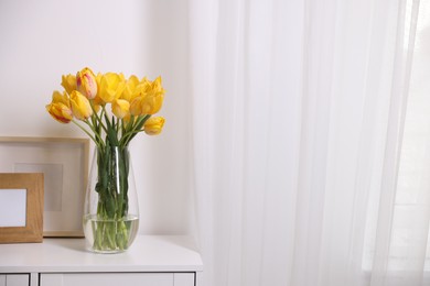 Photo of Bouquet of beautiful tulips and picture frames on table near white wall. Space for text