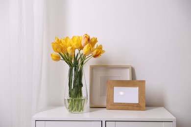 Photo of Bouquet of beautiful tulips and picture frames on table near white wall