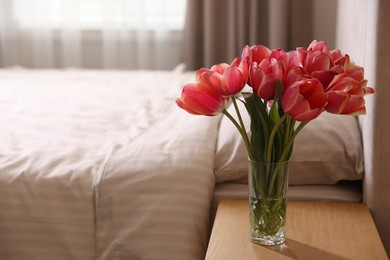 Photo of Bouquet of beautiful tulips on side table in bedroom. Space for text