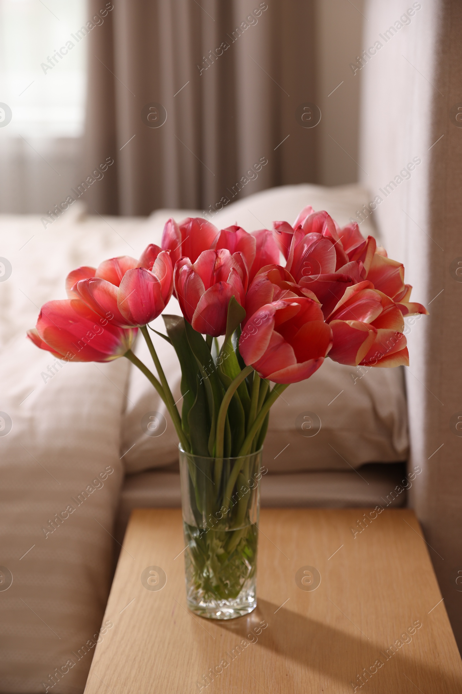 Photo of Bouquet of beautiful tulips on side table in bedroom