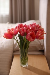 Photo of Bouquet of beautiful tulips on side table in bedroom