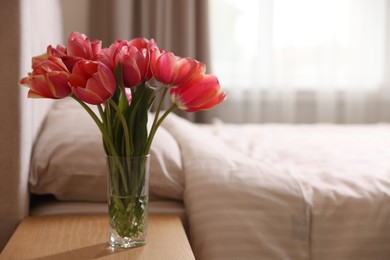 Photo of Bouquet of beautiful tulips on side table in bedroom. Space for text
