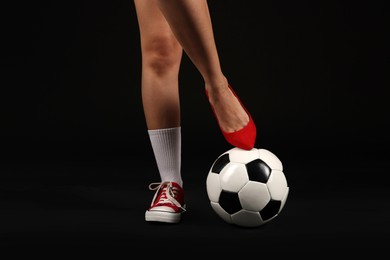 Photo of Woman in high heeled shoe and sneaker with soccer ball on dark background, closeup