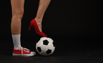 Photo of Woman in high heeled shoe and sneaker with soccer ball on dark background, closeup. Space for text