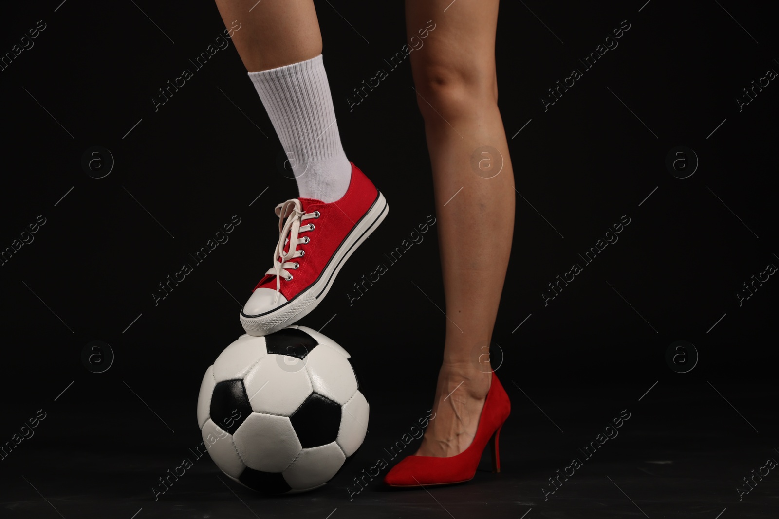 Photo of Woman in high heeled shoe and sneaker with soccer ball on dark background, closeup