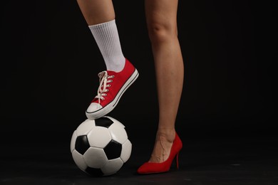 Photo of Woman in high heeled shoe and sneaker with soccer ball on dark background, closeup