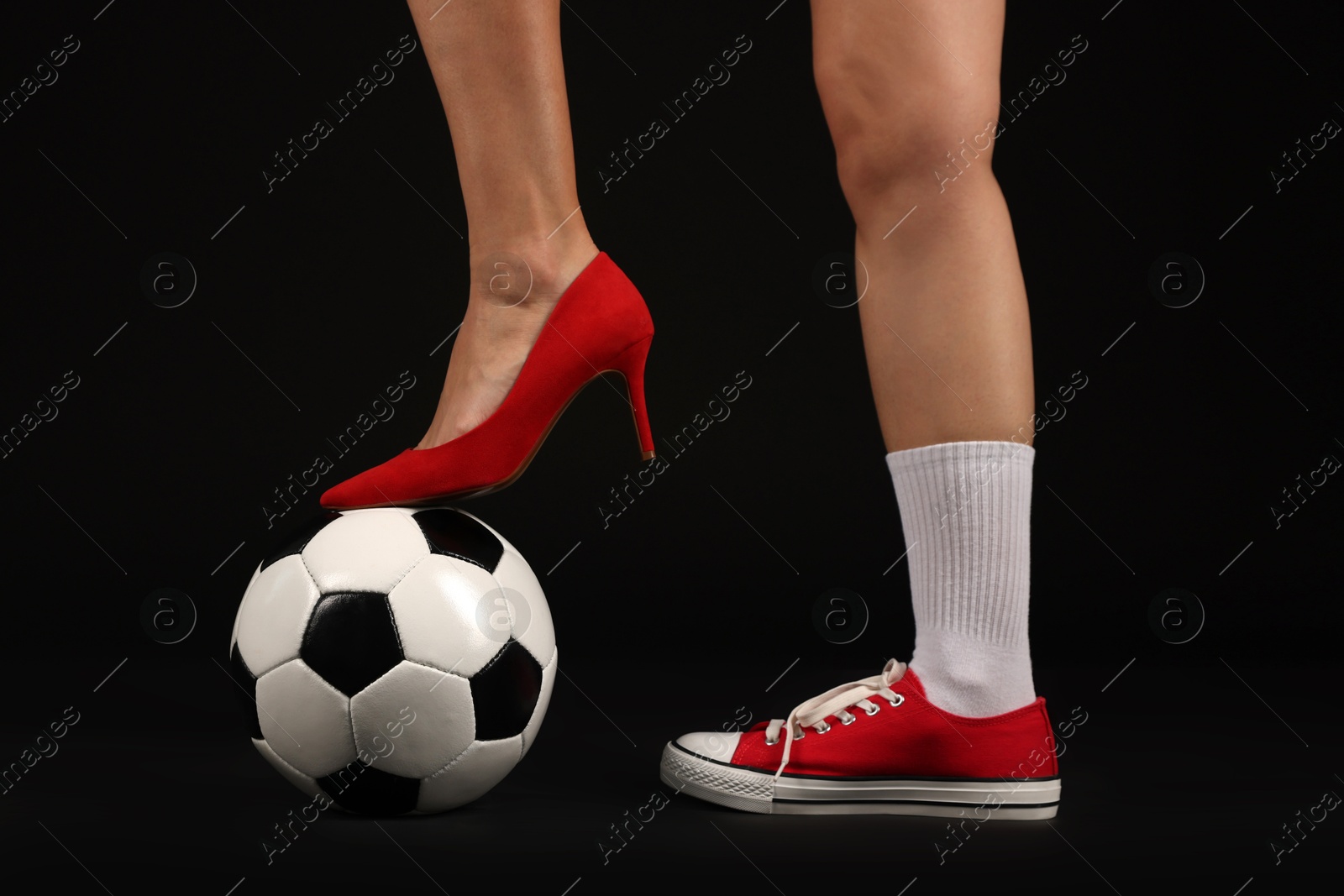 Woman in high heeled shoe and sneaker with soccer ball on dark background, closeup Photo of Woman in high heeled shoe and sneaker with soccer ball on dark background, closeup