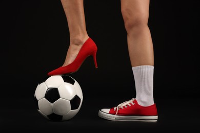 Photo of Woman in high heeled shoe and sneaker with soccer ball on dark background, closeup