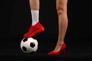 Photo of Woman in high heeled shoe and sneaker with soccer ball on dark background, closeup