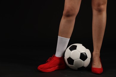 Photo of Woman in high heeled shoe and sneaker with soccer ball on dark background, closeup