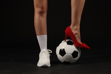 Photo of Woman in high heeled shoe and sneaker with soccer ball on dark background, closeup