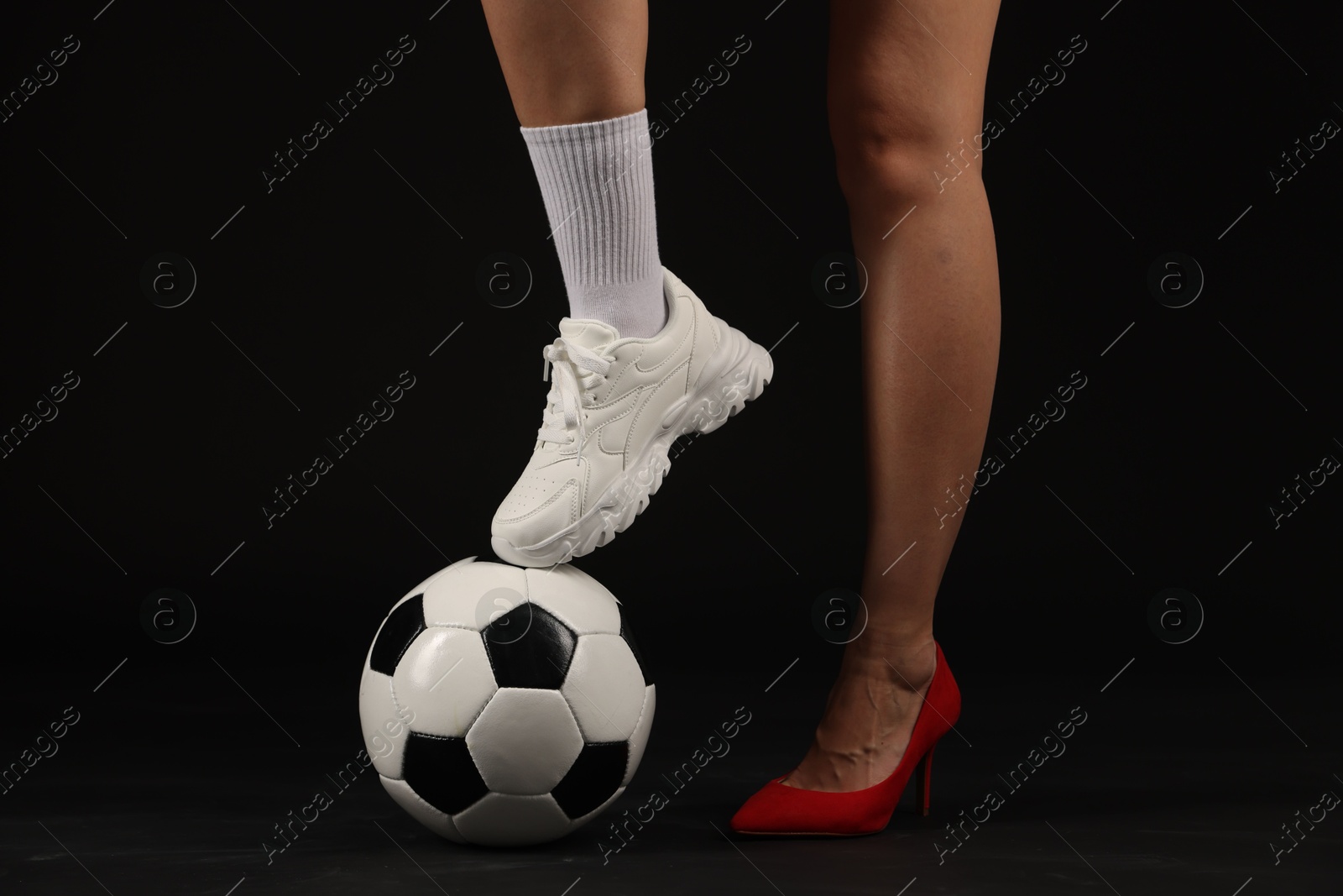 Photo of Woman in high heeled shoe and sneaker with soccer ball on dark background, closeup