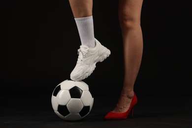 Photo of Woman in high heeled shoe and sneaker with soccer ball on dark background, closeup