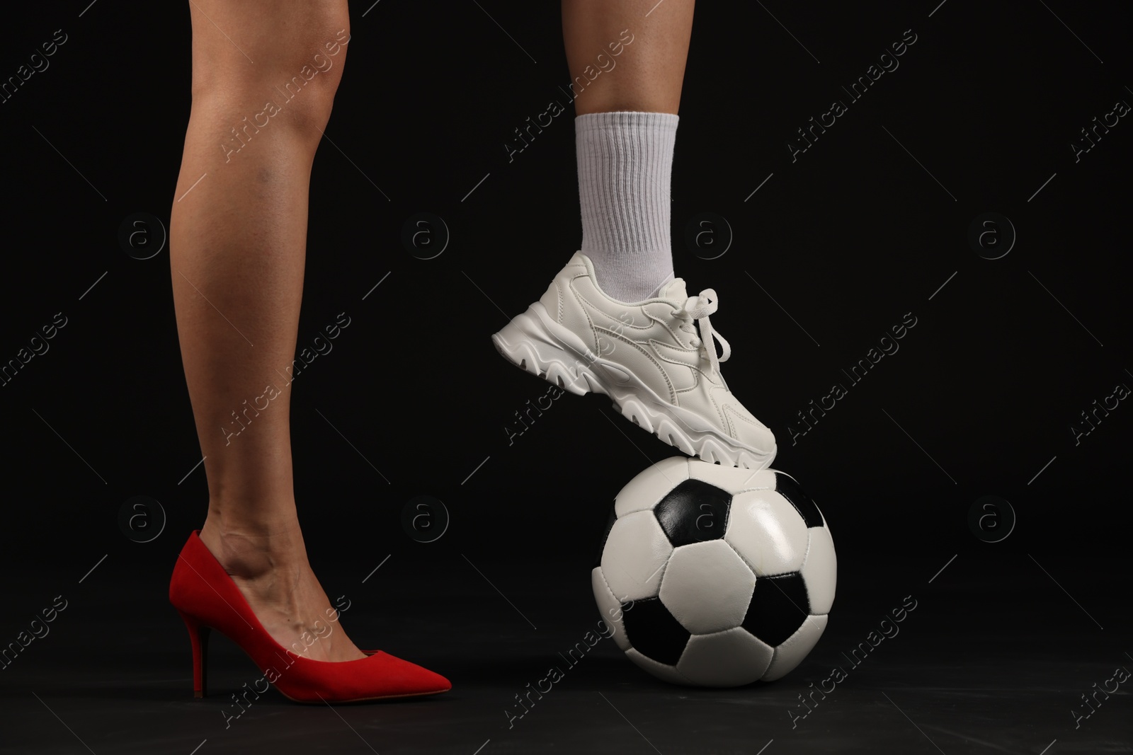 Photo of Woman in high heeled shoe and sneaker with soccer ball on dark background, closeup