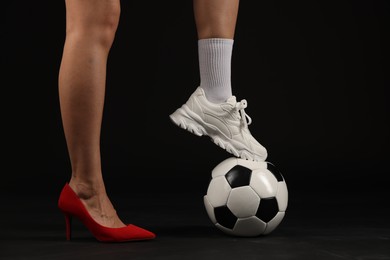 Photo of Woman in high heeled shoe and sneaker with soccer ball on dark background, closeup