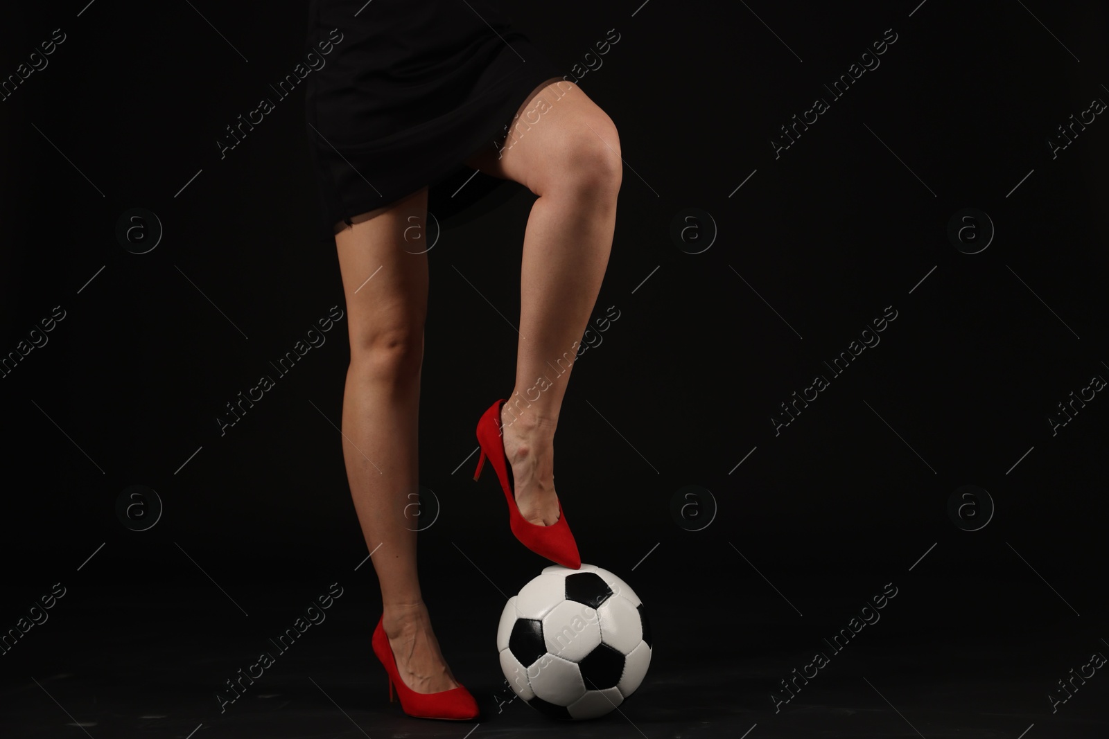 Photo of Woman in high heeled shoes with soccer ball on dark background, closeup