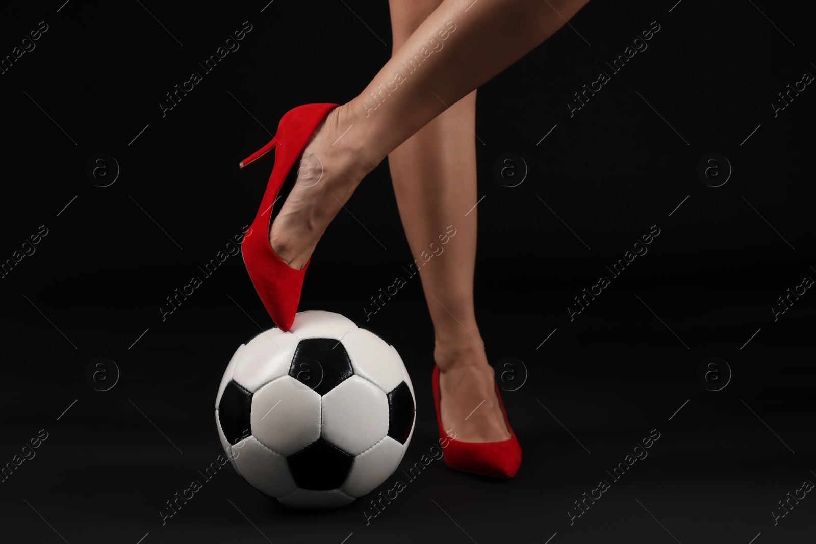 Photo of Woman in high heeled shoes with soccer ball on dark background, closeup