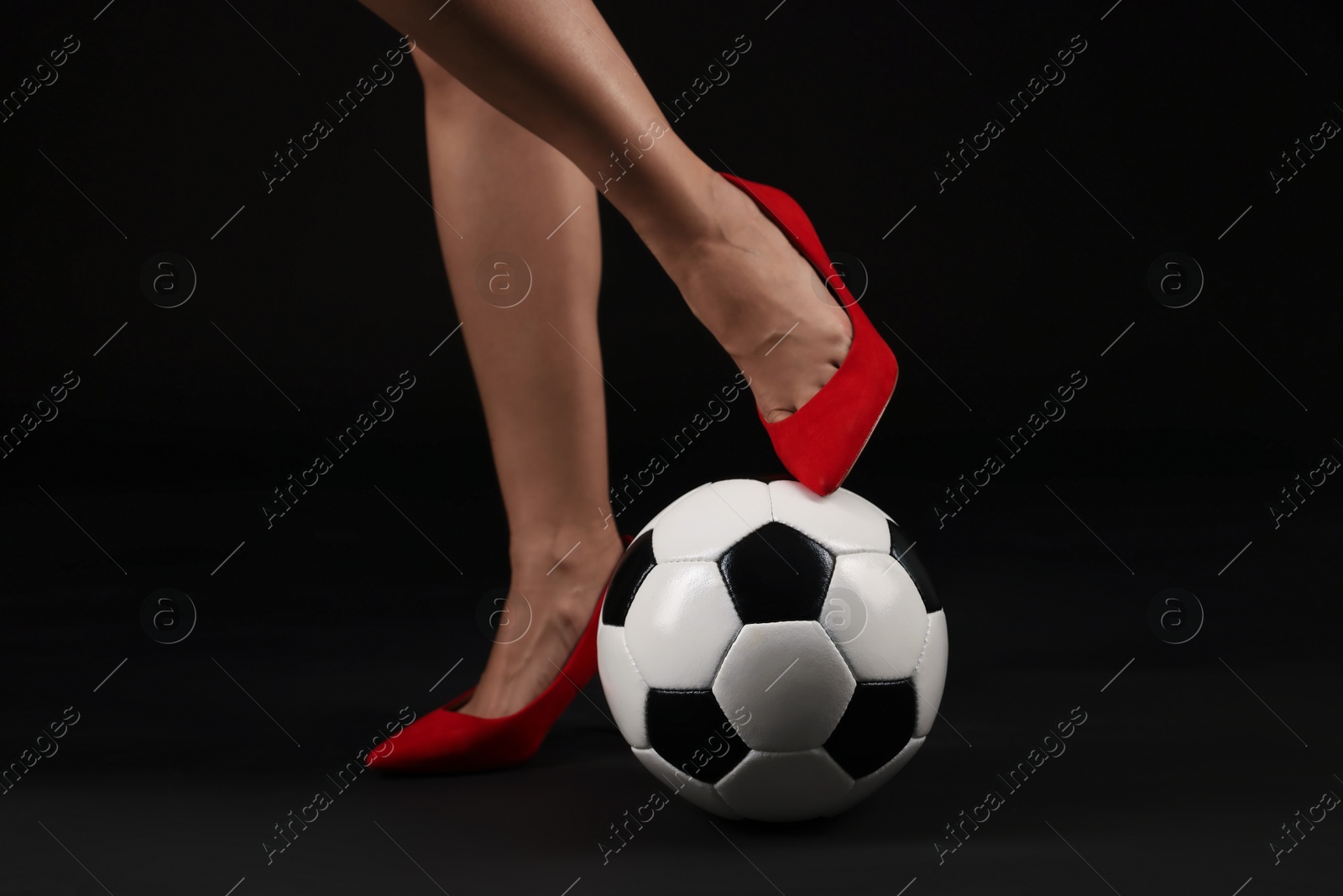 Photo of Woman in high heeled shoes with soccer ball on dark background, closeup