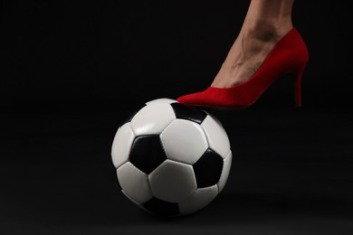 Photo of Woman in high heeled shoe with soccer ball on dark background, closeup