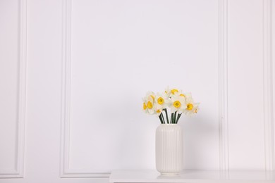 Photo of Beautiful daffodils in vase on table near white wall at home, space for text