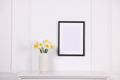 Photo of Beautiful daffodils in vase on dresser and picture frame at home