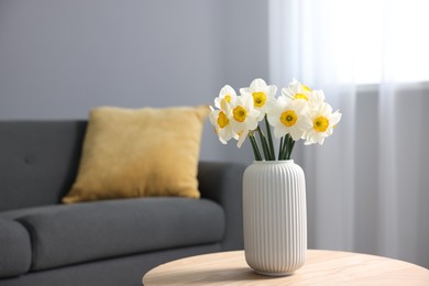 Photo of Beautiful daffodils in vase on wooden table indoors, space for text