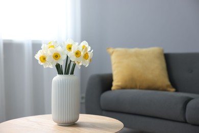 Photo of Beautiful daffodils in vase on wooden table indoors, space for text
