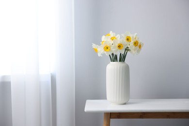 Photo of Beautiful daffodils in vase on white table indoors, space for text
