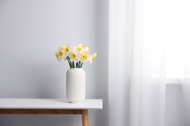 Photo of Beautiful daffodils in vase on white table indoors, space for text