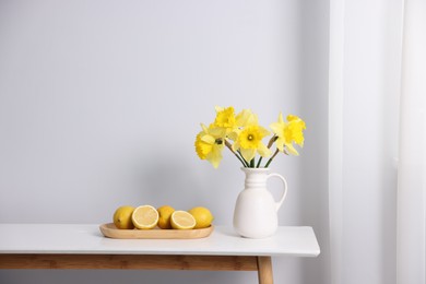 Photo of Beautiful daffodils in vase and lemons on white table indoors