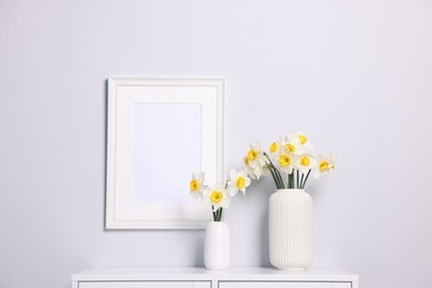 Photo of Beautiful daffodils in vases on cabinet and picture frame at home