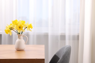 Photo of Beautiful daffodils in vase on wooden table at home, space for text