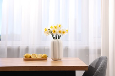Photo of Beautiful daffodils in vase and lemons on wooden table at home