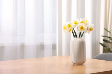 Photo of Beautiful daffodils in vase on wooden table at home, space for text