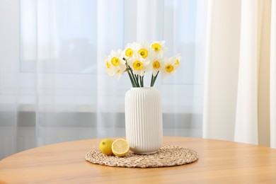 Photo of Beautiful daffodils in vase and lemons on wooden table at home