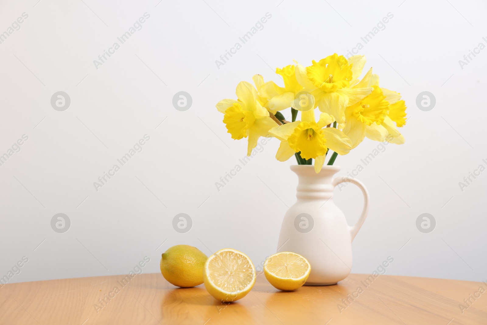 Beautiful daffodils in vase and lemons on wooden table near white wall at home Photo of Beautiful daffodils in vase and lemons on wooden table near white wall at home
