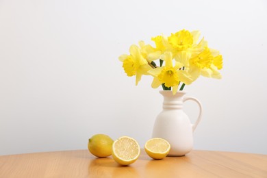 Photo of Beautiful daffodils in vase and lemons on wooden table near white wall at home